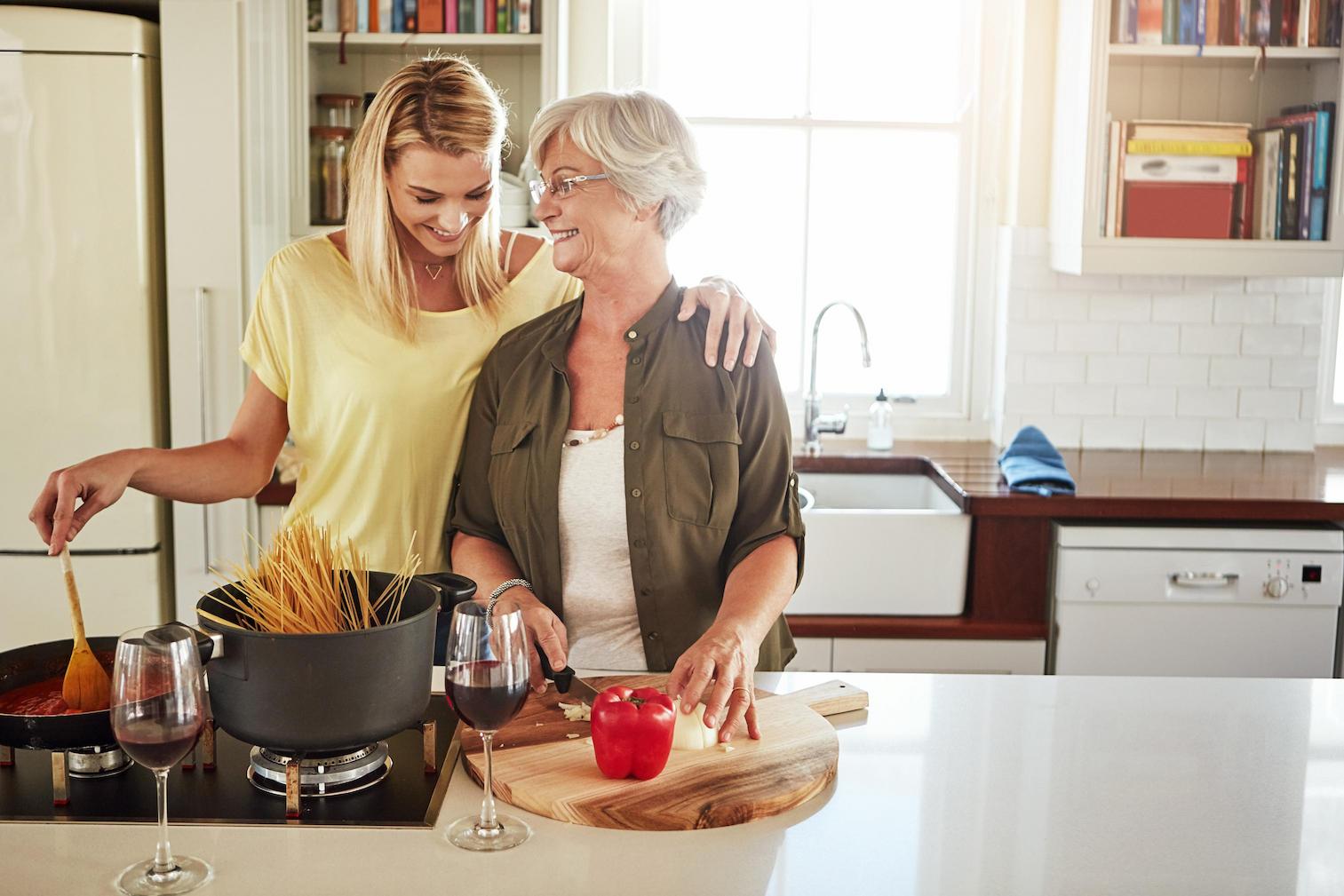 vrouw slaat in de keuken liefdevol haar arm om haar oudere moeder terwijl ze voor haar moeder kookt
